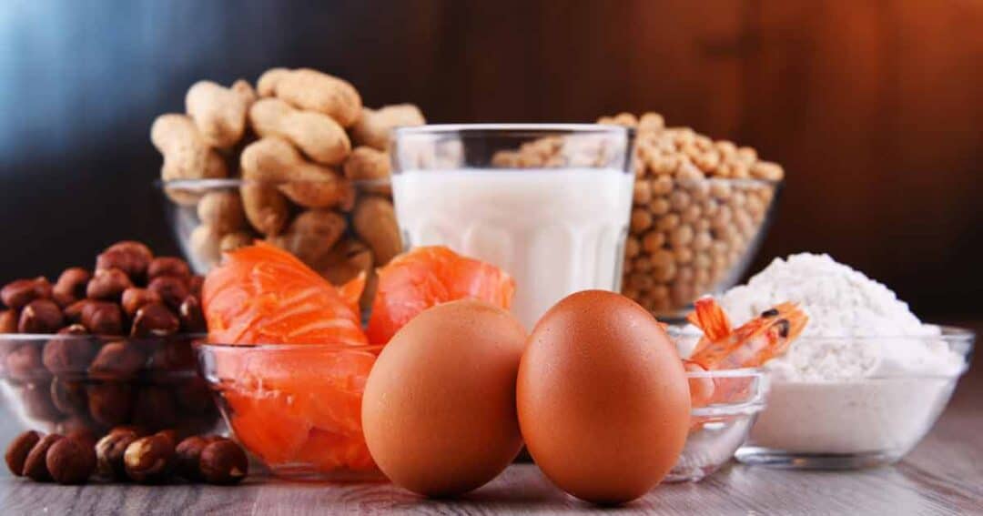 Safe Food Substitutions for Top 9 Food Allergens 1 Various foods are displayed, including peanuts, milk, soybeans, hazelnuts, salmon, shrimp, and eggs, arranged on a wooden surface. These items are commonly associated with food allergies.