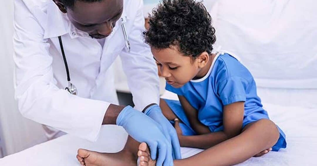 Health Equity in Allergies, Asthma and Immunology 14 A doctor wearing gloves examines the foot of a young child sitting on a medical bed. The child is in a blue gown and seems focused on the examination. The setting appears to be a clinical environment.