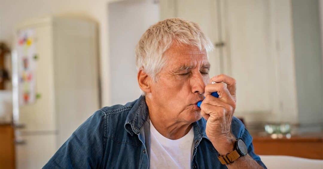 an elderly man using an asthma inhaler