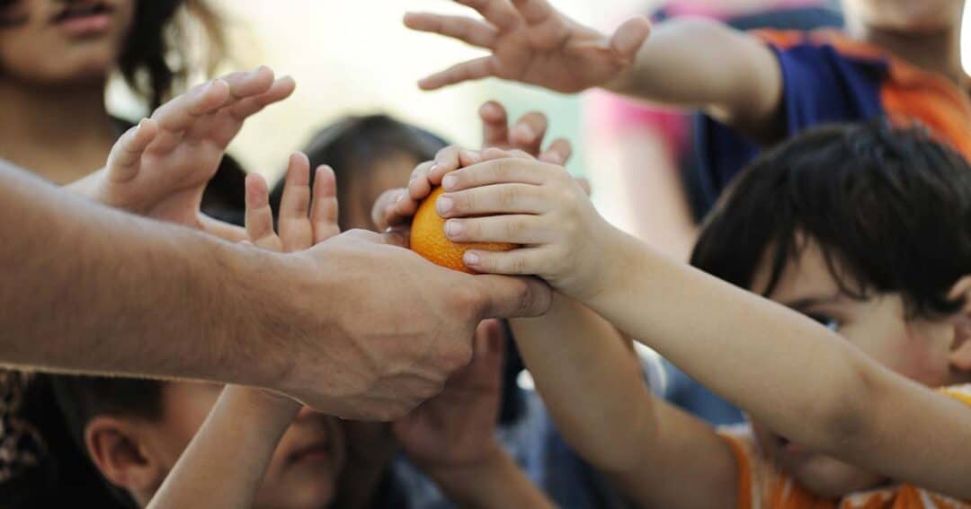 many hungry children's hands reaching for one orange