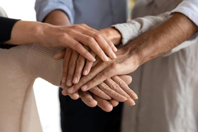 A group of people stacking their hands together in a gesture of teamwork and unity. The image focuses on the hands overlapping each other, symbolizing collaboration and mutual support.
