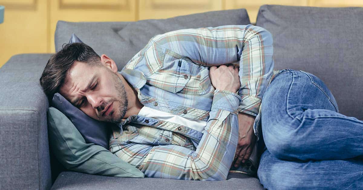 a man suffering abdominal pain lays in fetal position on a couch while holding his stomach