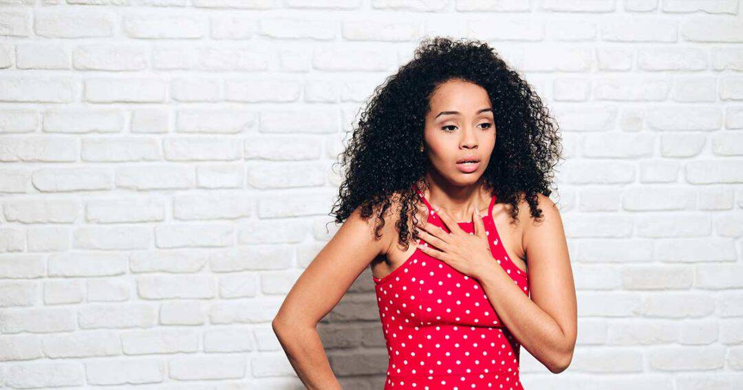 woman with curly hair holds her chest while having an asthma attack