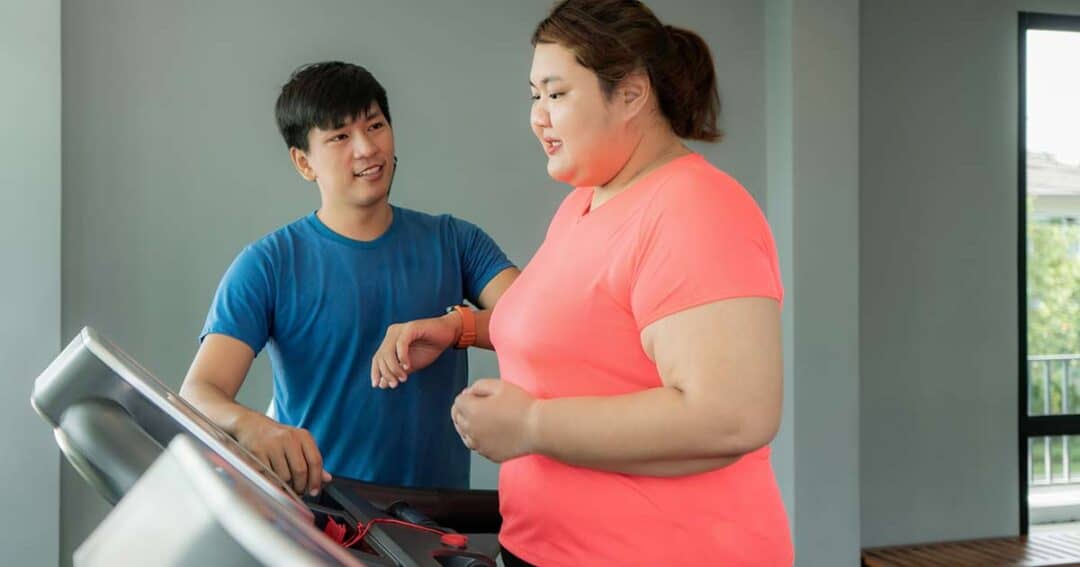 Woman working out on treadmill as her trainer looks on.
